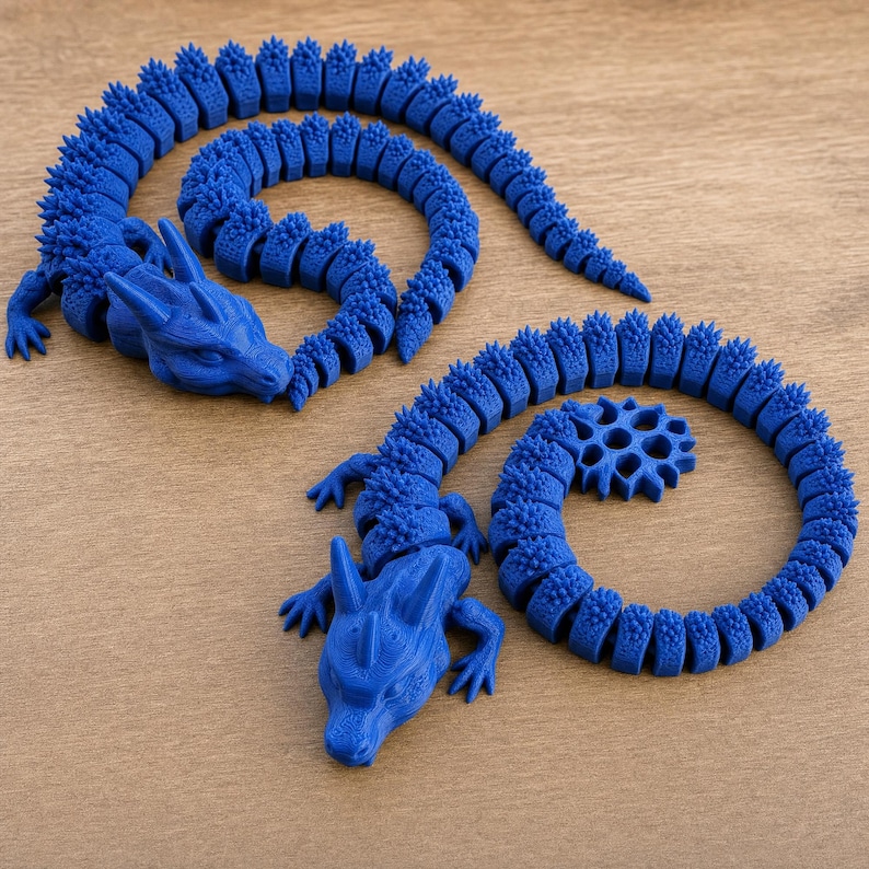 May include: Two articulated blue dragon figures with segmented bodies and spiky textures. Each dragon features a detailed head with horns, four small legs, and a long, flexible tail that curls into a circular shape, showcasing 3D printed construction.