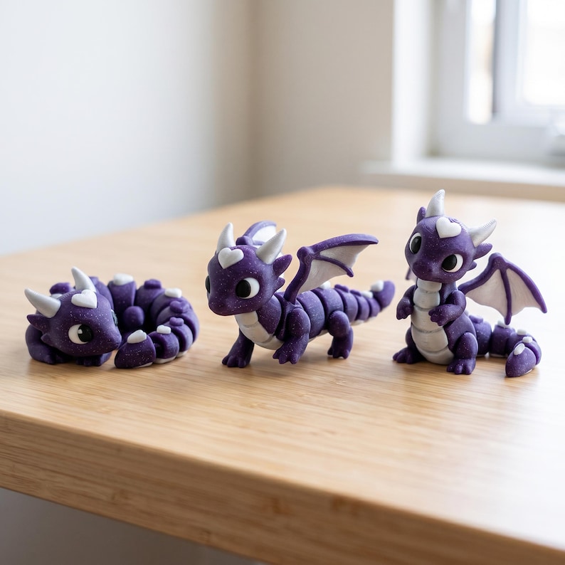 May include: Three purple dragon figurines with white accents. One dragon is curled in a ball, one stands on all fours with wings spread, and one sits upright. Each dragon features a white heart shape on its forehead and large black eyes.