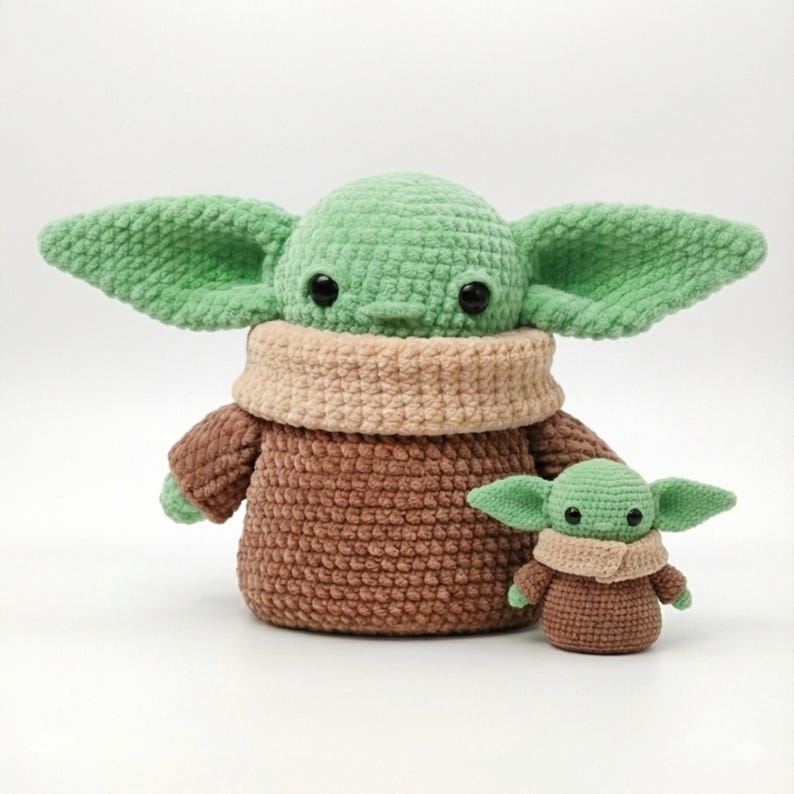 Op de afbeelding: Twee gehaakte figuren van een personage met grote oren, groene huid en zwarte ogen. De grotere figuur is bruin met een beige kraag en groene oren. De kleinere figuur is een miniatuurversie van de grotere.