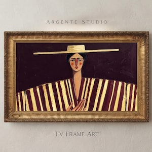 Może przedstawiać: Oprawiony obraz zatytułowany Argente Studio TV Frame Art przedstawiający osobę w kapeluszu z szerokim rondem i w pasiastym ubraniu z pionowymi kasztanowymi i kremowymi liniami na ciemnym tle, w ozdobnej złotej ramie.