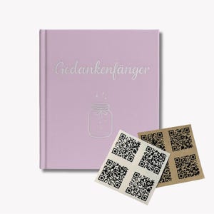 Könnte beinhalten: Ein lila Notizbuch mit dem Text "Gedankenfänger" und einer Gläser-Illustration. Mehrere QR-Code-Aufkleber liegen neben dem Notizbuch. Das Notizbuch hat einen weichen Einband und ein schlichtes Design.