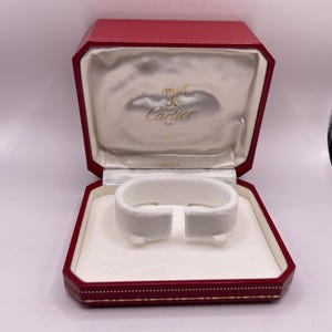 Może przedstawiać: Biały ceramiczny kubek z czarnym uchem i napisem "But First, Coffee" pogrubioną, czarną czcionką. Kubek jest ustawiony na rozmytym tle, sugerującym przytulne otoczenie.