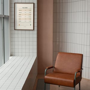 May include: A framed wall art print titled TEA GUIDE featuring a table of tea types, temperatures, and steeping times, displayed in a room with white tiled walls and a brown leather armchair with a dark metal frame near a large window.