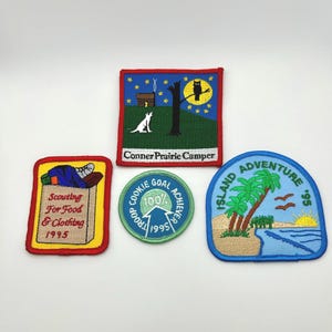 May include: Five embroidered patches with various designs. One patch features a dog, a tree, and the text "Conner Prairie Camper." Another says "Scouting For Food & Clothing 1995." Other patches include "Cookie Goal Achiever 1995" and "Island Adventure '95."