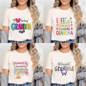 May include: Four cream-coloured t-shirts with colourful text designs. The shirts feature phrases like "I love being GRANDMA," "LIFE'S GREATEST GIFT MOM GRANDMA GRANDMA," "Powered by Grandma's LOVE," and "Blessed GRANDMA." Each shirt has a unique graphic.