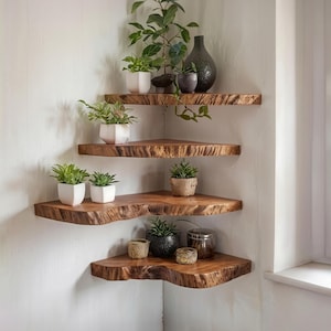 May include: Four wooden corner shelves with a natural edge, mounted on a white wall. The shelves display potted plants, a dark vase, and decorative containers. The shelves are made of wood, with a rustic aesthetic.