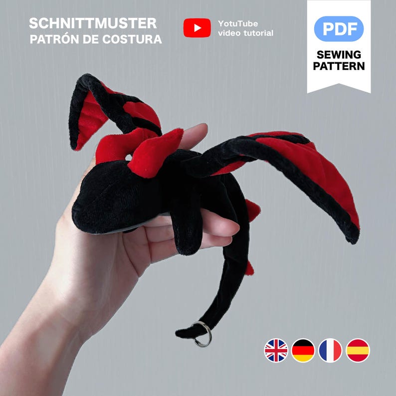 Peut inclure: Un jouet en peluche en forme de dragon noir et rouge avec de grandes ailes et une queue incurv&eacute;e. Le dragon a un anneau argent&eacute; attach&eacute; &agrave; sa queue. Le texte de l'image indique "SCHNITTMUSTER PATR&Oacute;N DE COSTURA" et "PDF SEWING PATTERN".
