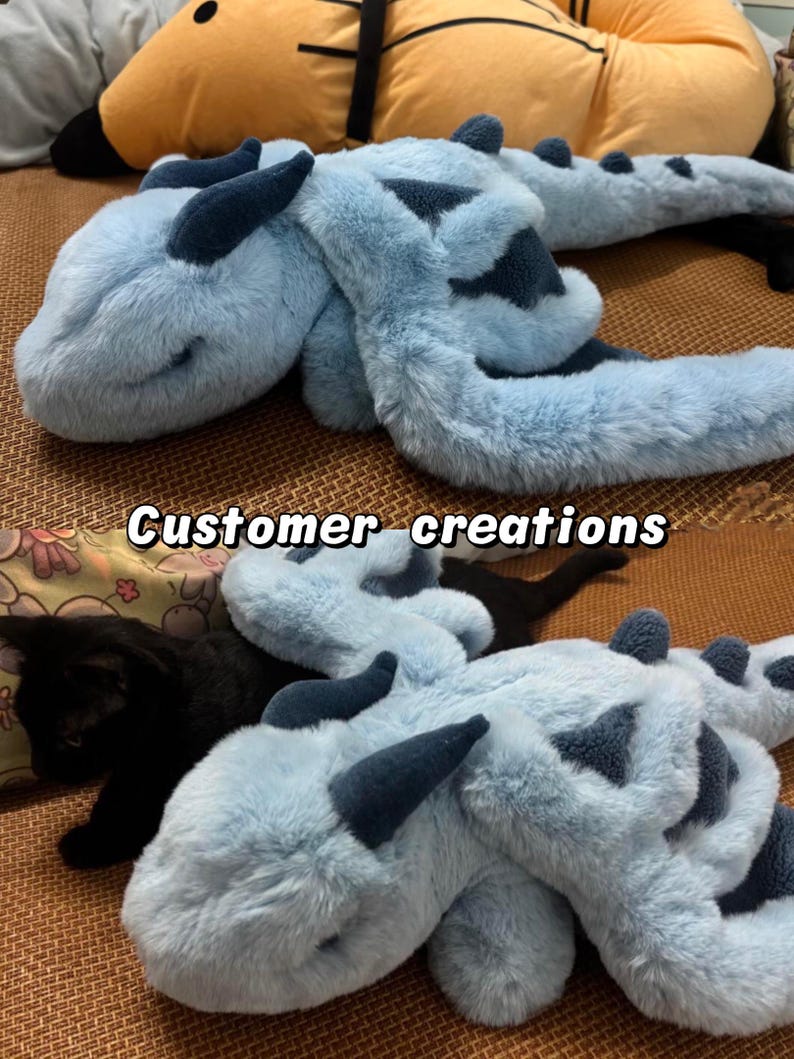 Peut inclure: Une peluche en forme de dragon bleu clair avec des d&eacute;tails bleu fonc&eacute;, comme les cornes et les motifs. Le jouet est doux et duveteux, avec un long corps et une queue. Le texte "Customer creations" est visible.