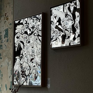 Puede incluir: Dos obras de arte abstractas enmarcadas con un diseño espejado y arremolinado en tonos negros, blancos y grises. Los marcos son de color marrón oscuro y la obra está montada en una pared gris texturizada.