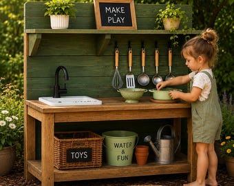 Könnte beinhalten: Eine hölzerne Outdoor-Spielküche mit grüner Rückwand, weißem Waschbecken und schwarzem Wasserhahn. Sie verfügt über hängende Küchenutensilien, ein Schild mit der Aufschrift MAKE PLAY, einen Korb mit TOYS-Beschriftung, einen Eimer mit WATER & FUN und eine Gießkanne.