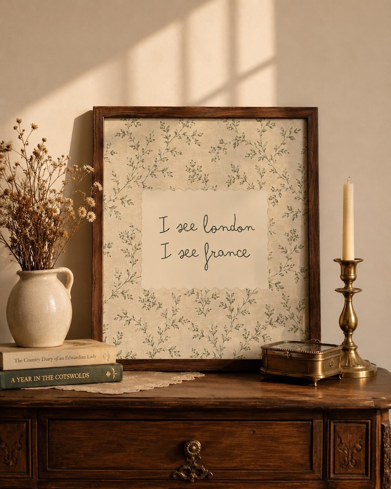 May include: A framed wall art piece featuring a cream-colored center with the text I see london I see france in black script, surrounded by a green botanical pattern on a beige background, all enclosed in a dark brown wooden frame.