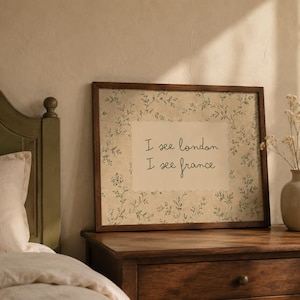 May include: A rectangular framed wall art piece featuring a cream-colored center panel with the black text I see london I see france, surrounded by a border of delicate green botanical illustrations on a textured, off-white background.