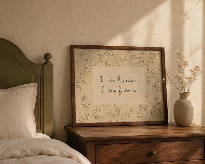 May include: A rectangular framed wall art piece featuring a cream-colored center panel with the black text I see london I see france, surrounded by a border of delicate green botanical illustrations on a textured, off-white background.
