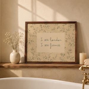 May include: A rectangular wall art print in a dark wood frame featuring a beige background with a delicate green botanical vine pattern and a central cream-colored rectangle containing the black handwritten text I see london I see france.