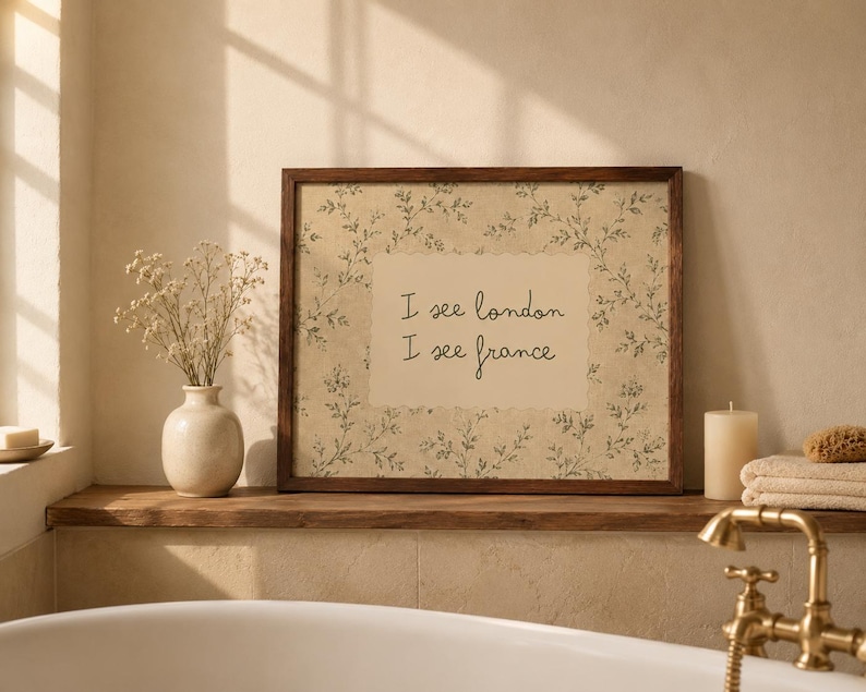 May include: A rectangular wall art print in a dark wood frame featuring a beige background with a delicate green botanical vine pattern and a central cream-colored rectangle containing the black handwritten text I see london I see france.