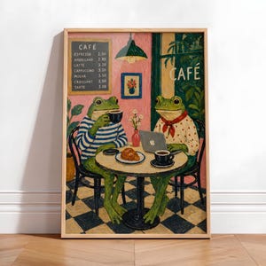 Może przedstawiać: Oprawiony wydruk przedstawia dwie antropomorficzne żaby w kawiarni. Jedna żaba nosi koszulę w paski i pije kawę, druga używa laptopa. Menu zawiera napis "CAFE" z cenami kawy i ciast. Scena rozgrywa się w kawiarni.