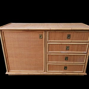 May include: A light brown bamboo cabinet with a woven front door and four drawers. The cabinet has brass hardware and a rectangular shape. The cabinet is made of bamboo and has a natural finish.