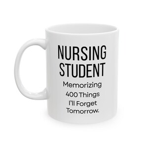 May include: White ceramic mug with a curved handle. The mug features the text "NURSING STUDENT" in a bold, black font, followed by "Memorizing 400 Things I'll Forget Tomorrow." A humorous gift for nursing students.