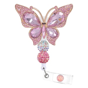 May include: A pink and gold butterfly-shaped badge reel. The butterfly has pink rhinestone wings and body. Below the butterfly are three decorative beaded spheres in pink and iridescent colors. A clear plastic badge holder is attached.