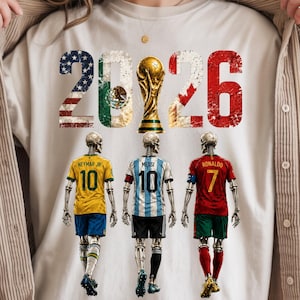 May include: A cream-colored t-shirt featuring the text 2026 with flag patterns and a gold trophy. Below, three skeletons wear soccer jerseys: a yellow number 10, a light blue and white striped number 10, and a red number 7, representing soccer players.