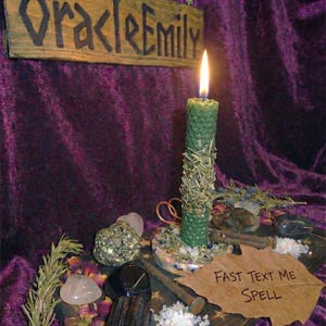 Puede incluir: Una vela verde encendida con una superficie texturizada, adornada con hierbas secas, se encuentra sobre un soporte decorativo. La imagen incluye cristales, hierbas y un letrero que dice "Fast Text Me Spell". Un letrero de madera arriba dice "Oracle Emily".