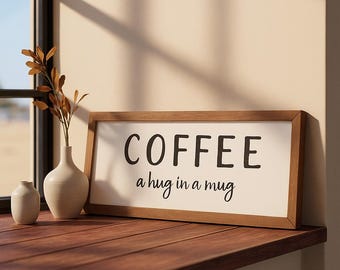 May include: A rectangular wooden sign with the words "COFFEE a hug in a mug" in black lettering. The sign is on a wooden surface, next to a window. A small vase with a plant is on the left.
