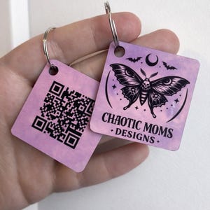 May include: Two square keychains with silver rings. One keychain has a QR code, the other features a black moth design with a skull, bats, and the text "CHAOTIC MOMS + DESIGNS" on a pink and purple background.