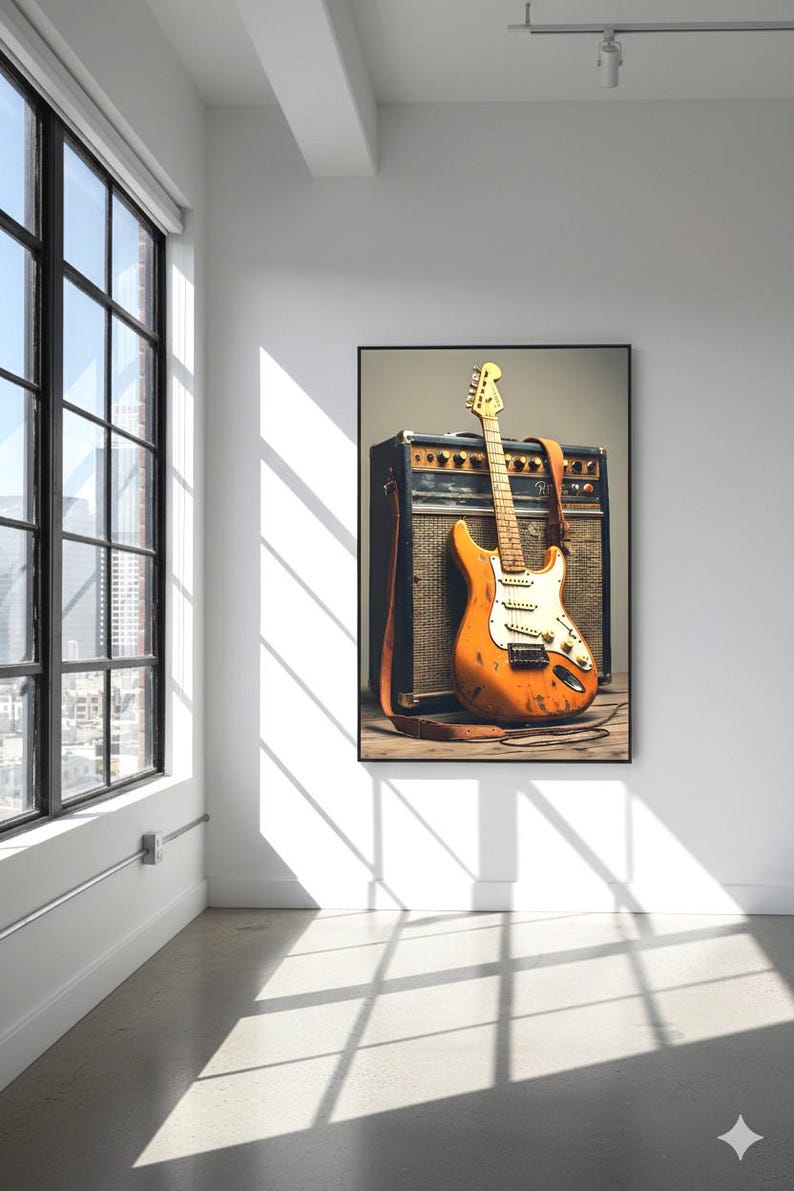 May include: An orange electric guitar with a white pickguard and a brown leather strap leans against a black and brown amplifier. The guitar has a worn appearance. The image is framed and hangs on a white wall.