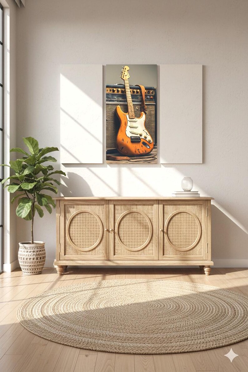May include: An orange electric guitar with a white pickguard and a brown strap leans against a black amplifier. The guitar is the focal point of a framed artwork above a wooden cabinet with woven door panels. A potted plant and a round jute rug complete the scene.