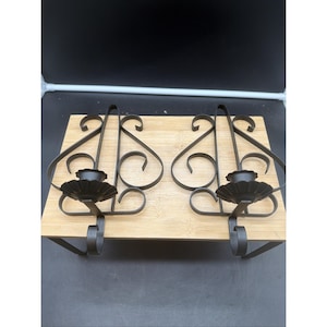 May include: A pair of dark brown metal wall sconces featuring intricate scrollwork designs and scalloped candle cups. Each sconce has a flat back plate with decorative metal loops and a curved base, designed for mounting candles securely on a wall.