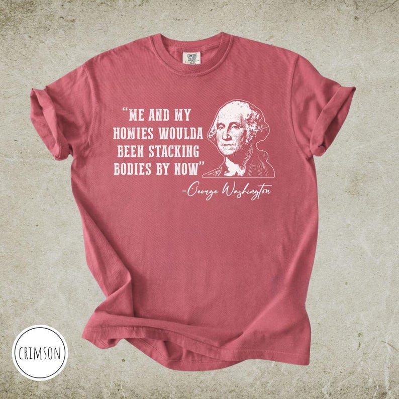 May include: Crimson-colored t-shirt with the quote "ME AND MY HOMIES WOULDA BEEN STACKING BODIES BY NOW" and a portrait of George Washington. The quote is in white, as is the name of George Washington.