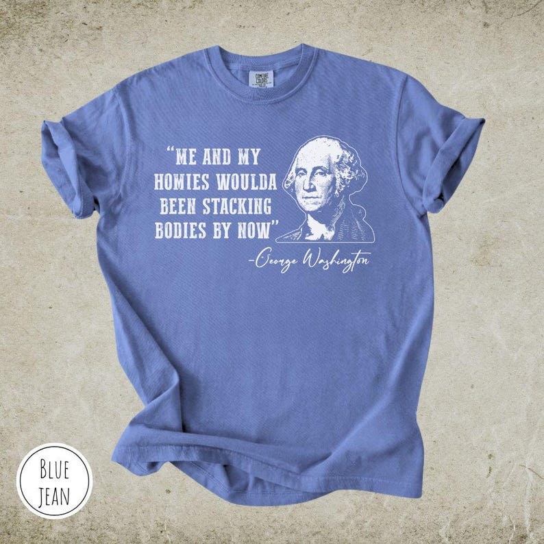 May include: A blue jean colored t-shirt with the quote "ME AND MY HOMIES WOULDA BEEN STACKING BODIES BY NOW" and a portrait of George Washington. The shirt also has the words "BLUE JEAN" in a circle.
