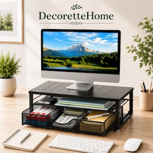 May include: A black metal monitor stand with a perforated top surface and a pull-out mesh drawer. The drawer contains a white calculator, pens, and notebooks. The stand supports a computer monitor displaying a mountain landscape. Text reads DecoretteHome.