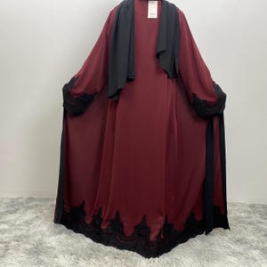 以下が含まれることがあります： 黒いショールと黒いレースのトリムが付いた、バーガンディ色のドレス。 ドレスは、黒いレースのカフスと黒いレースの裾が付いた長袖です。 黒いショールは肩にかけられています。