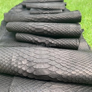 May include: Close-up of several rolls of black reptile skin, showcasing a textured, scaled pattern. The rolls are stacked, revealing the intricate details of the material. The image includes the text "Hafiz Reptile".