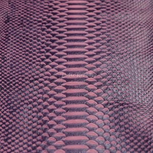 Può includere: Primo piano di un motivo a pelle di serpente viola strutturato. Le squame sono in rilievo e creano un effetto tridimensionale. Il colore passa da un viola intenso a una tonalità più chiara e rosata al centro, creando un effetto sfumato. Il motivo è simmetrico.