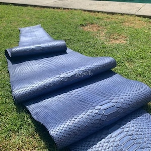 May include: A roll of blue leather with a snakeskin pattern lies on green grass. The leather is a solid blue color with a textured surface. The word "Reptile" is visible on the leather.
