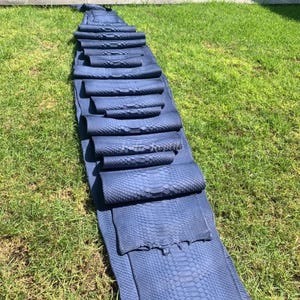 May include: A collection of rolled, blue-grey leather hides, arranged on green grass. The hides have a textured, scale-like pattern. The arrangement suggests a display of leather goods or materials for crafting.