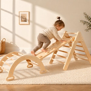May include: A wooden climbing frame set, including an arch, ramp, and triangle. A toddler is climbing the ramp. The set is on a cream rug. A woven basket and a framed picture are in the background.