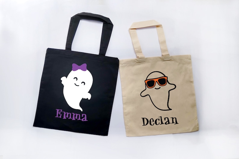 May include: Two Halloween-themed tote bags. One black bag features a white ghost with a purple bow and the name "Emma" in purple. The other is tan with a ghost wearing orange sunglasses and the name "Declan".