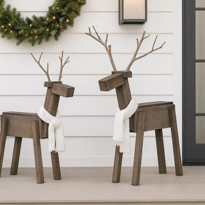 May include: Two reindeer figures constructed from brown stained wood planks. Each figure features a rectangular body, four straight legs, a block-shaped head, and branch-like antlers. Both reindeer wear a white knitted scarf around their necks.