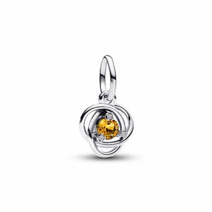 May include: A silver charm with a central yellow gemstone, encircled by a swirling, openwork design. Three small, clear stones are set around the yellow gem. The charm has a loop for attaching to a bracelet or necklace.