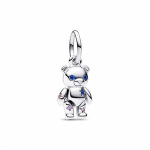 May include: A silver teddy bear charm with blue gem eyes and star-shaped gems in pink and blue. The charm has a loop for attaching to a bracelet or necklace. The bear is standing upright.