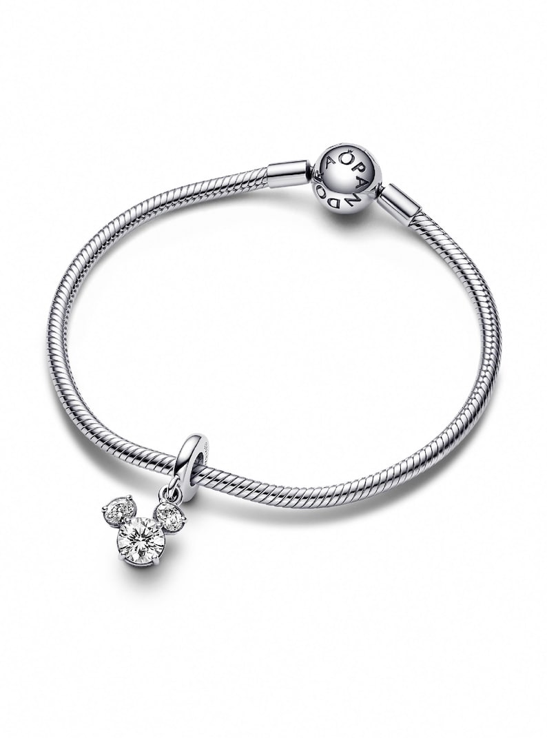 A silver-toned bracelet with a charm featuring a Mickey Mouse design and a small crystal pendant.