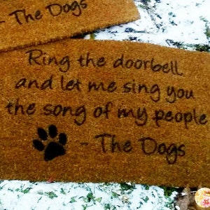 May include: Two rectangular doormats made of a natural fiber material. Each mat has the text "Ring the doorbell and let me sing you the song of my people - The Dogs" and a paw print.