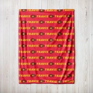 May include: Red fleece blanket with a repeating pattern of yellow "TRAVIS" text and a yellow arrowhead logo with the letters "KC".