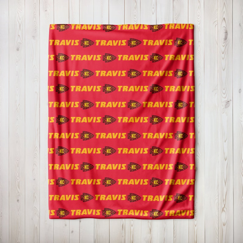 May include: Red fleece blanket with a repeating pattern of yellow "TRAVIS" text and a yellow arrowhead logo with the letters "KC".