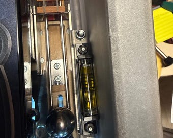 May include: Close-up of a pinball machine's interior, showcasing metallic components, a level, and a silver ball. The image includes the text "PROTEGO" and "SPELL HARD TO LIGHT". The level is filled with a yellow liquid.