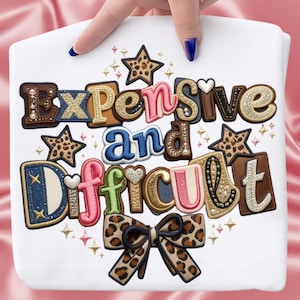 May include: White tote bag with the embroidered text "Expensive and Difficult" in various colors and textures. The design includes stars, a bow, and decorative embellishments.