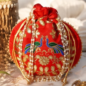 May include: A red drawstring pouch with gold trim and pearl accents. The pouch features embroidered peacocks and floral designs. A decorative accessory for special occasions.